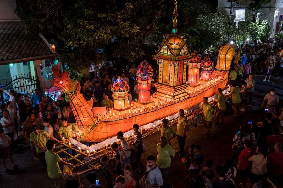 Locals carry a magnificent illuminated boat through the historic old town at dusk