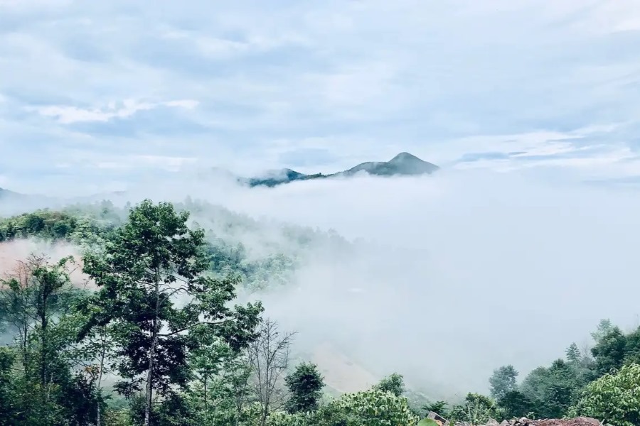 Fluffy clouds blanket the evergreen valleys around A Pa Chai, with the mountains from afar