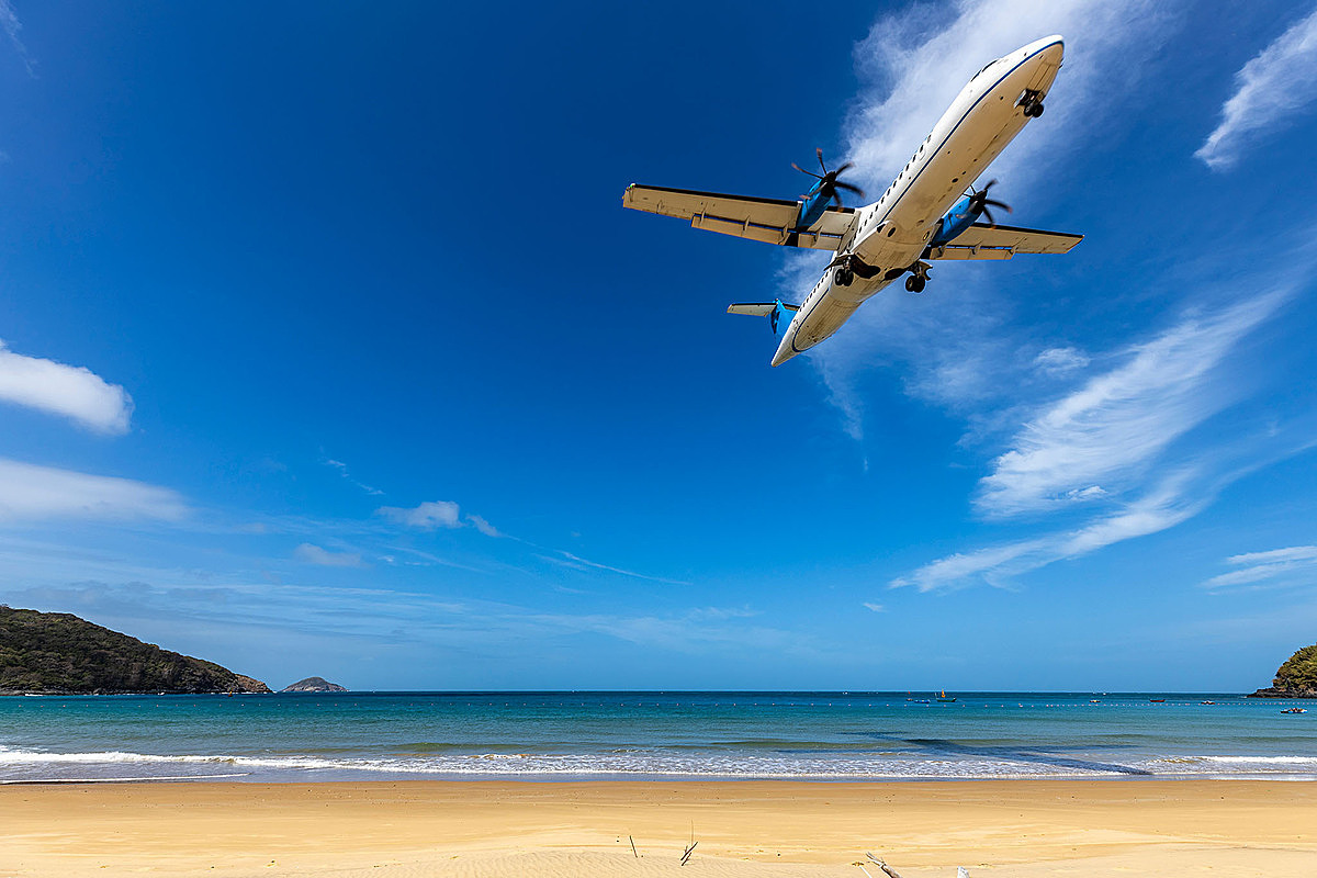 Tourists standing on the beach can clearly see the airplane flying right above their heads