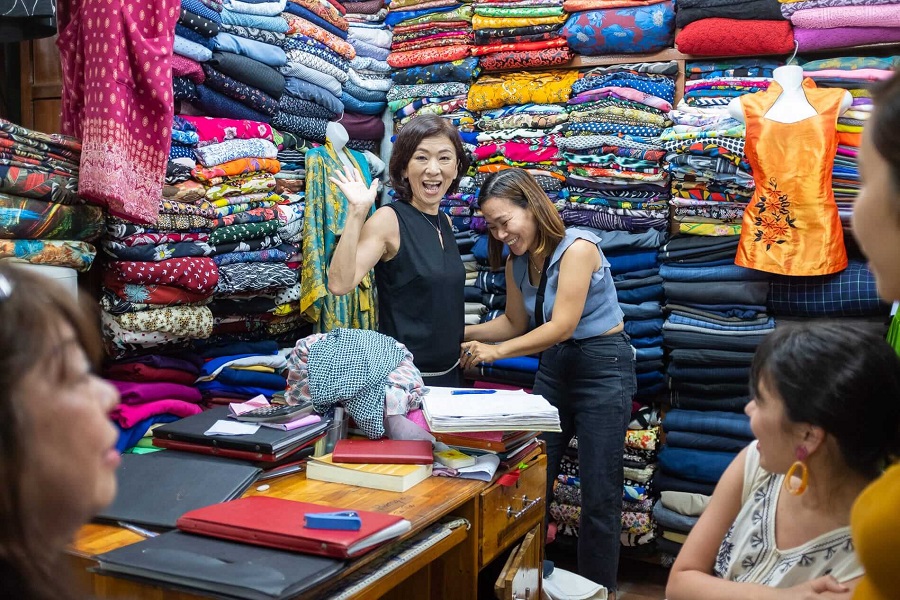 A joyful customer shares a laugh while getting measured at a tailor shop in Hoi An, Vietnam