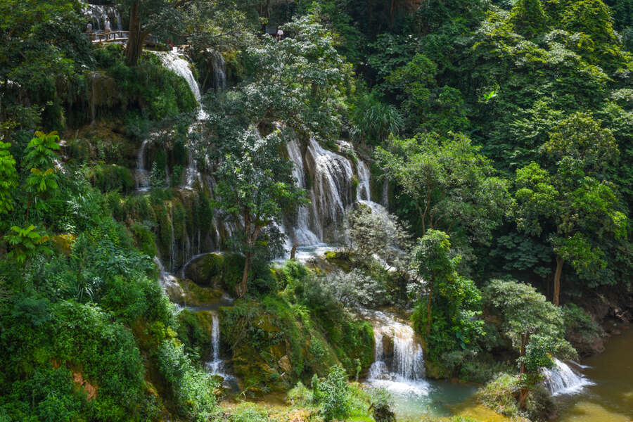 The white of the waterfall blends with the green of the mountains and forests