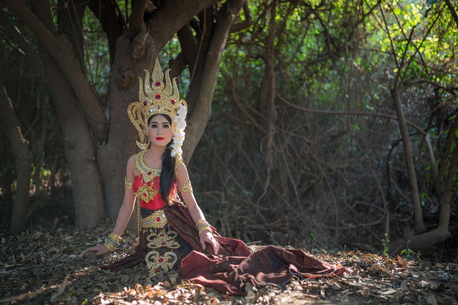 A graceful Apsara dancer in traditional attire sits amidst a serene forest landscape, exuding elegance.