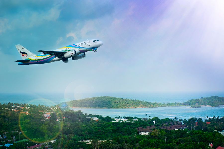 An airplane flies over the island of Koh Samui, Thailand, revealing a vibrant tropical landscape in the daylight.