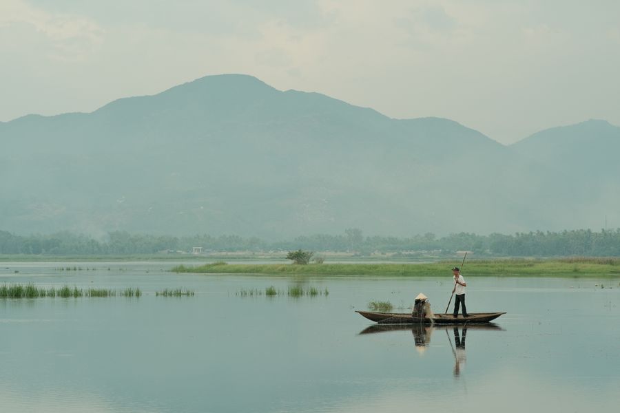 Two fishermen on a boat in the middle of a peaceful lake.