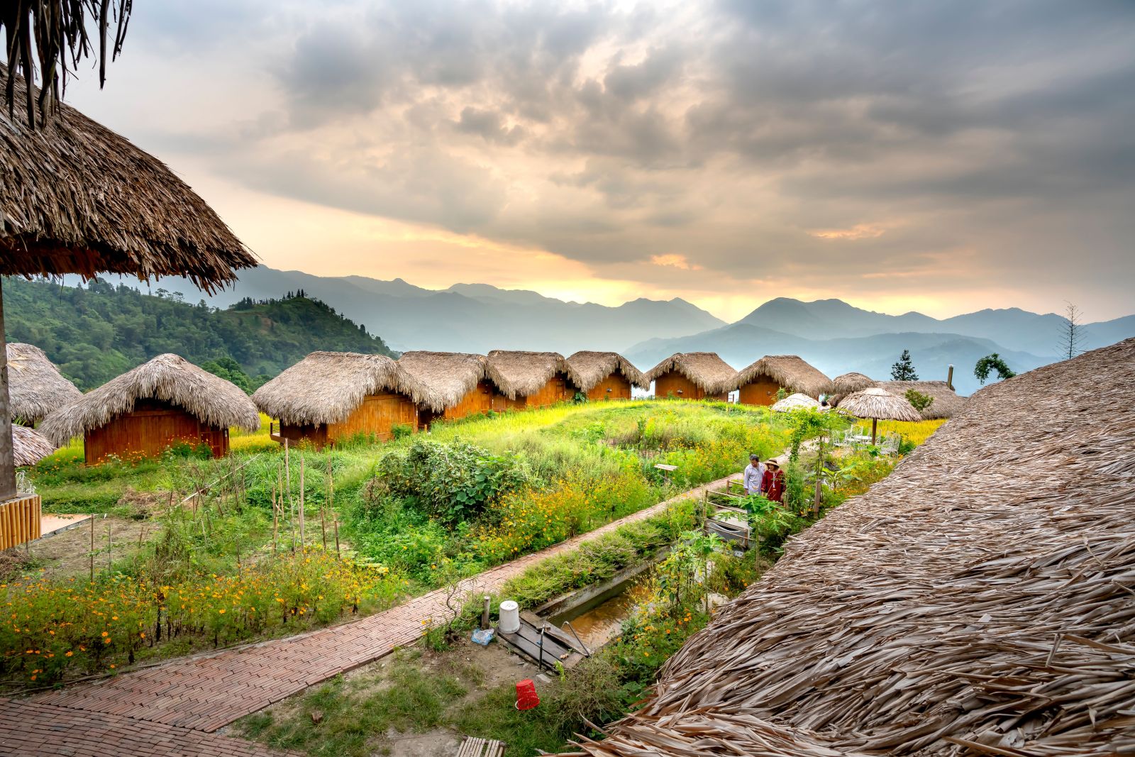 A beautiful village with thatched-roof huts nestled among lush green hills under a cloudy sky.
