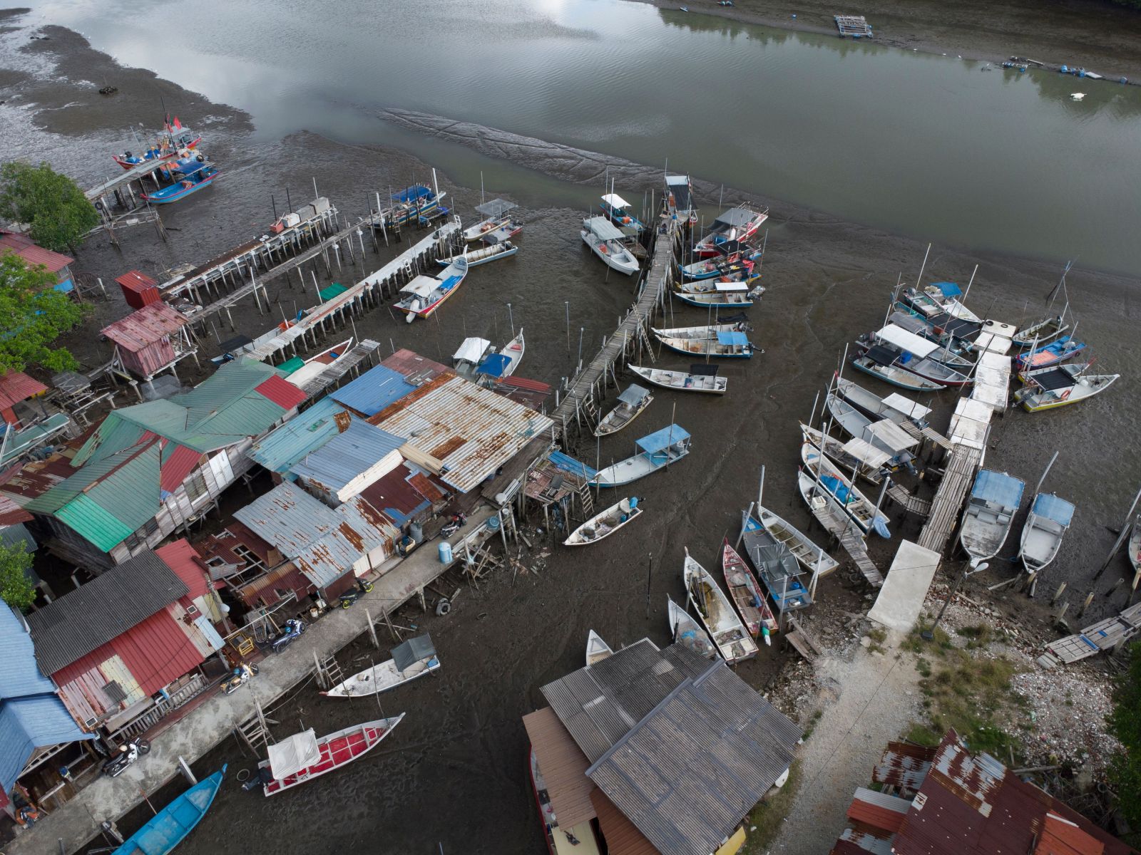 An aerial view of a Malaysian fishing village featuring colorful boats and a jetty at low tide.