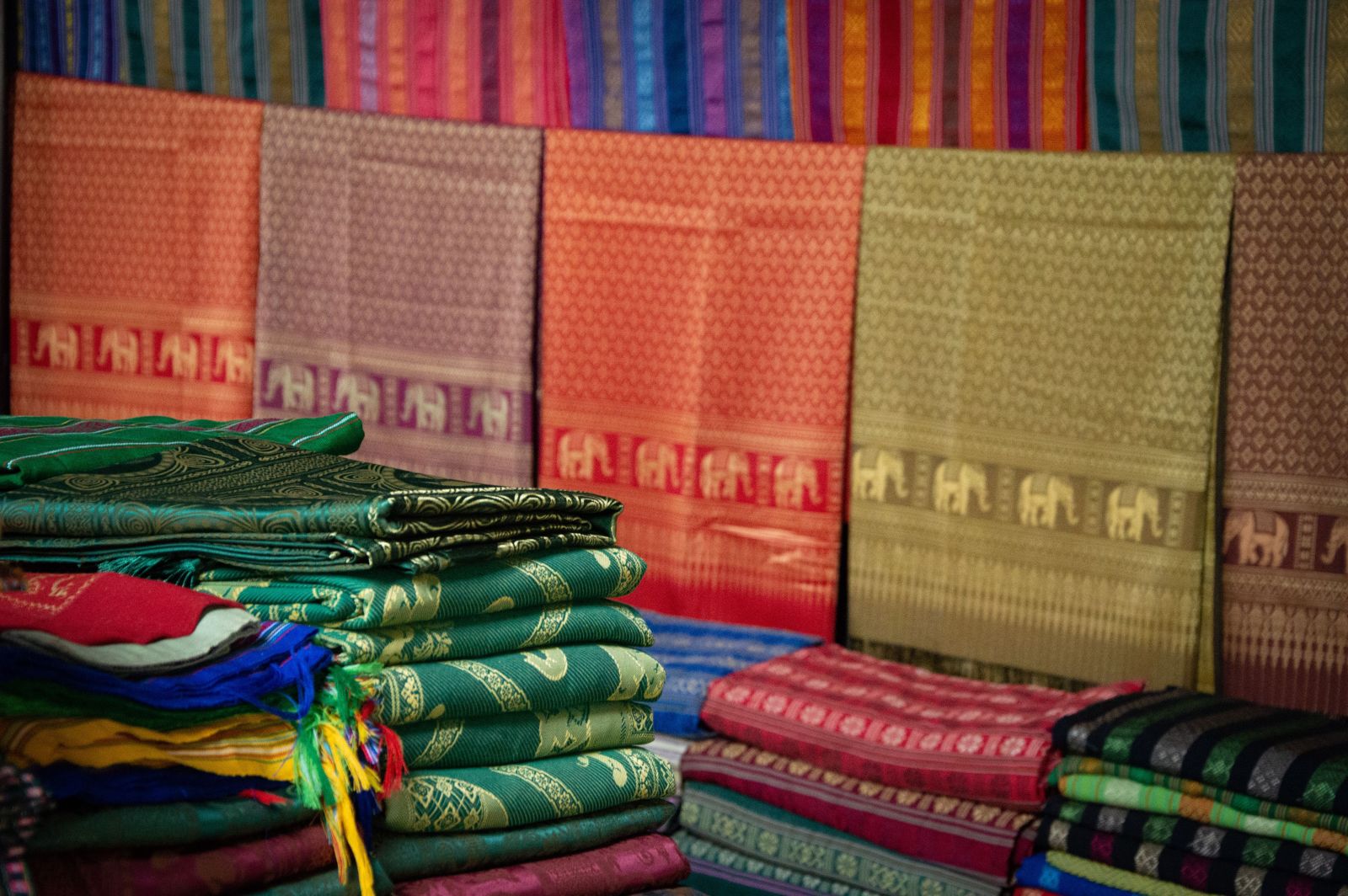 A wide array of colorful fabrics with intricate patterns is on display at a market