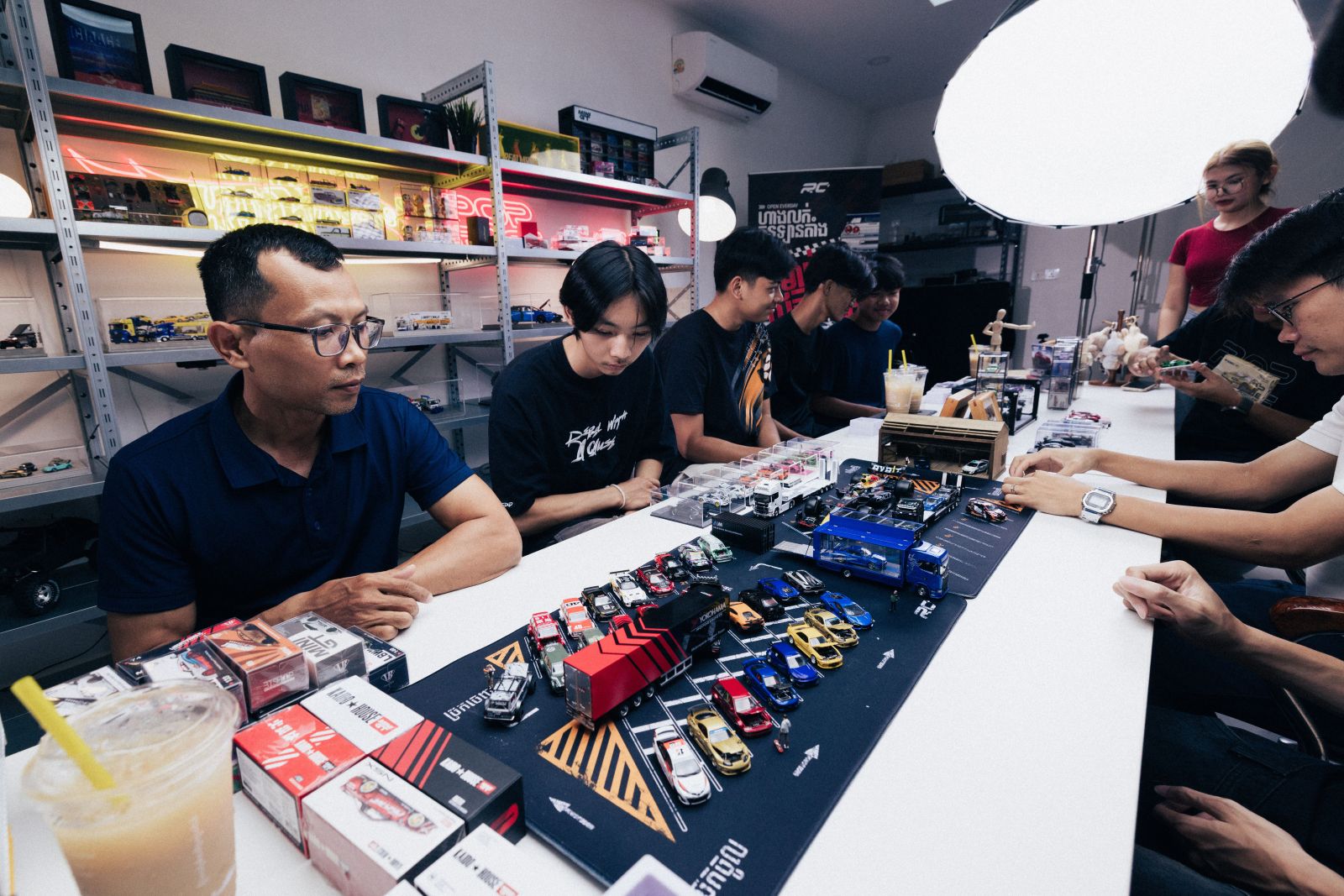 A group of model car enthusiasts are enjoying model cars in a brightly lit shop with shelves displaying them