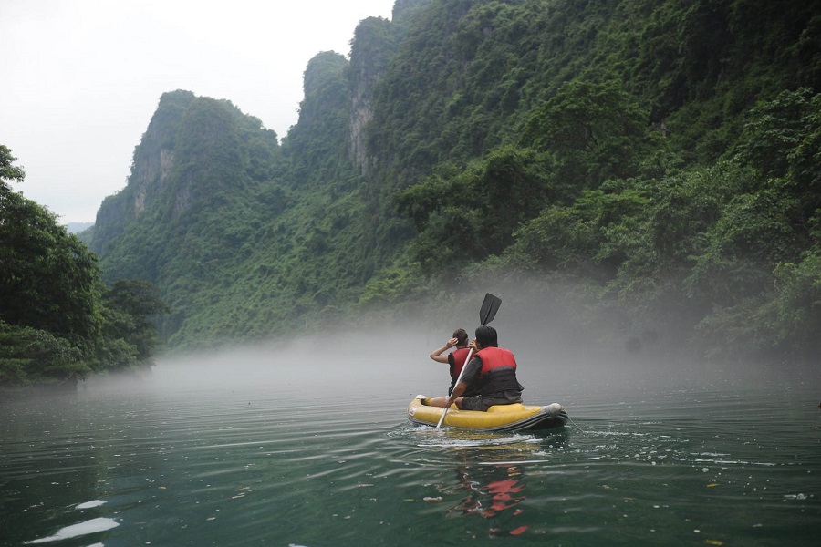 Two people kayak through the misty Chay River, surrounded by lush green mountains